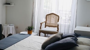 A bedroom with a bed, a chair, a TV, and a window with sheer curtains.