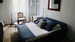 A bedroom with a bed, a chair, a desk, and a mirror.