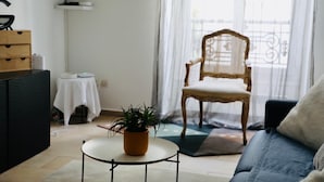 A living room with a sofa, a chair, a small table with a plant, a wooden cabinet, and a window with curtains.