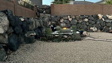 Un muro de piedra con una chimenea, suelo de grava y una palmera.