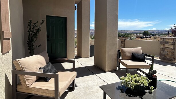 Un patio al aire libre con sofás color beige, una mesa de vidrio y plantas en macetas.