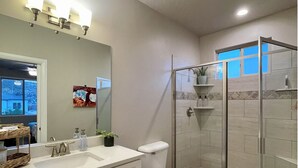 Un baño moderno con cabina de ducha de vidrio, un lavamanos blanco con espejo y un inodoro.