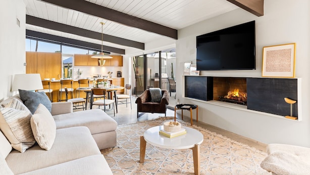 A modern living room with a fireplace, sofa, coffee table, and a kitchen area in the background. - 30+ Stay! Gorgeous Home W/Pool/Spa/Mtn Views (Palm Springs)