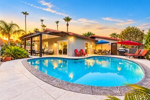 A swimming pool with a covered patio area, outdoor seating, and palm trees.