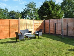 A fenced backyard with a patio area, outdoor furniture, and a wooden fence.