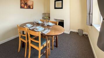 A dining room with a round table set for four, wooden chairs, a painting on the wall, a mirror, and a fireplace.