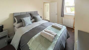 A neatly made bed with pillows and a blanket, a bedside table with a lamp, and a window with curtains.