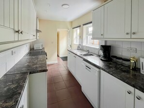 A kitchen with white cabinets, a black countertop, a coffee maker, and a window.