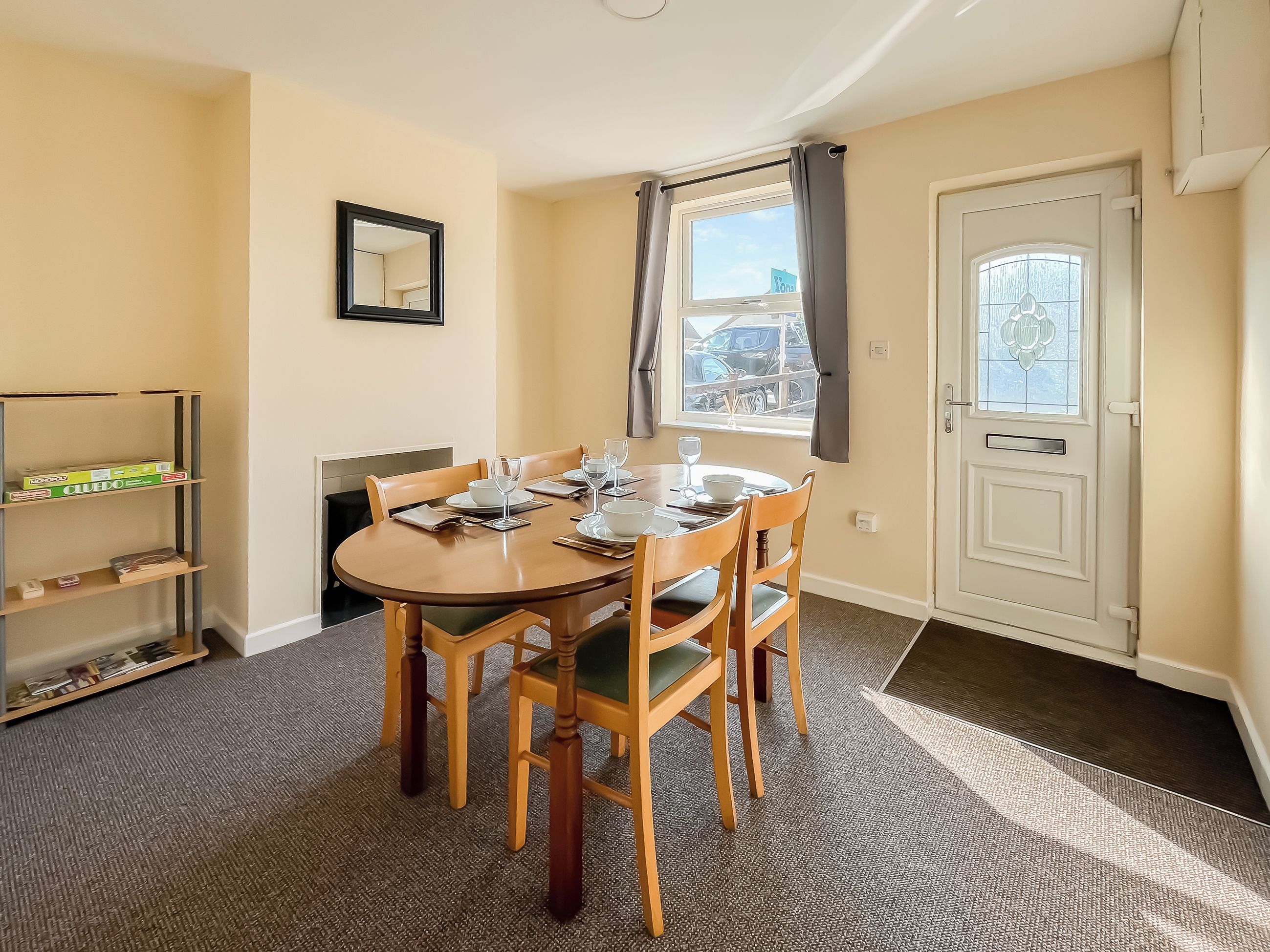 Un coin repas avec une table ronde, quatre chaises, une bibliothèque, une porte avec une fenêtre et un tableau encadré au mur.