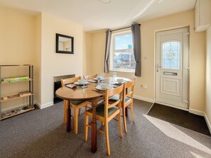 A dining area with a round table, four chairs, a bookshelf, a door with a window, and a framed picture on the wall.