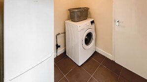 A laundry area with a washing machine, a basket on top, and a door. - 2 bedroom accommodation in Firsby (Firsby)