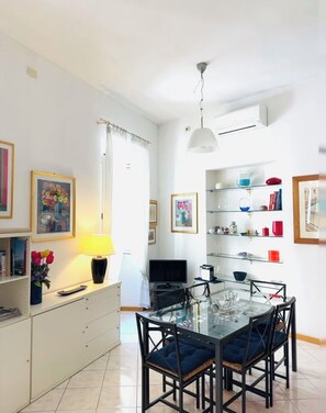 A modern dining area with a glass table and chairs, a television, and a white ceiling fan. - Elegant apartment in the heart of Rome - Spanish Steps (Roma)