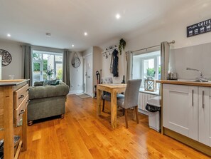 A cozy kitchen with wooden flooring, a dining area with a table and chairs, a sofa, and a view of the outdoors.