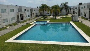 A modern pool area with a rectangular pool, surrounded by well-maintained grass and palm trees. - Departamento en Fraccionamiento Seguro

 (Yautepec de Zaragoza)