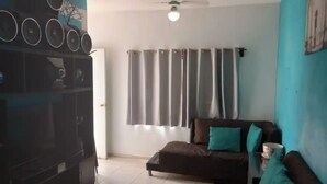 A living room with a dark brown sofa, teal cushions, a black entertainment unit, and a ceiling fan. - Departamento en Fraccionamiento Seguro

 (Yautepec de Zaragoza)