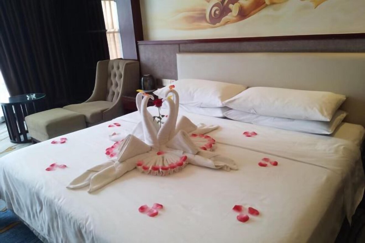A hotel room with a neatly made bed, a chair, a small table, and a painting on the wall.