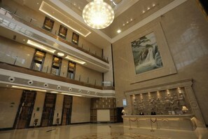 A spacious lobby with a high ceiling, a grand chandelier, and a large painting on the wall.