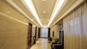 A hotel corridor with a marble floor, a seating area with chairs, and a large window with curtains. - Vienna International Hotel (Mount Emei Crystal Plaza Hotel) (Emeishan City)