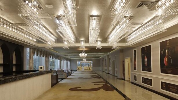 A long, elegant hallway with chandeliers, a marble floor, and framed pictures on the walls. - Vienna International Hotel (Mount Emei Crystal Plaza Hotel) (Emeishan City)