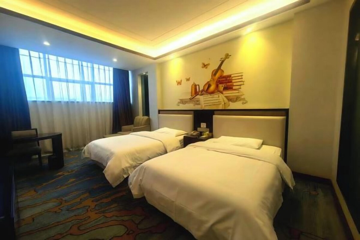 A hotel room with two beds, a desk, a chair, and a large window.