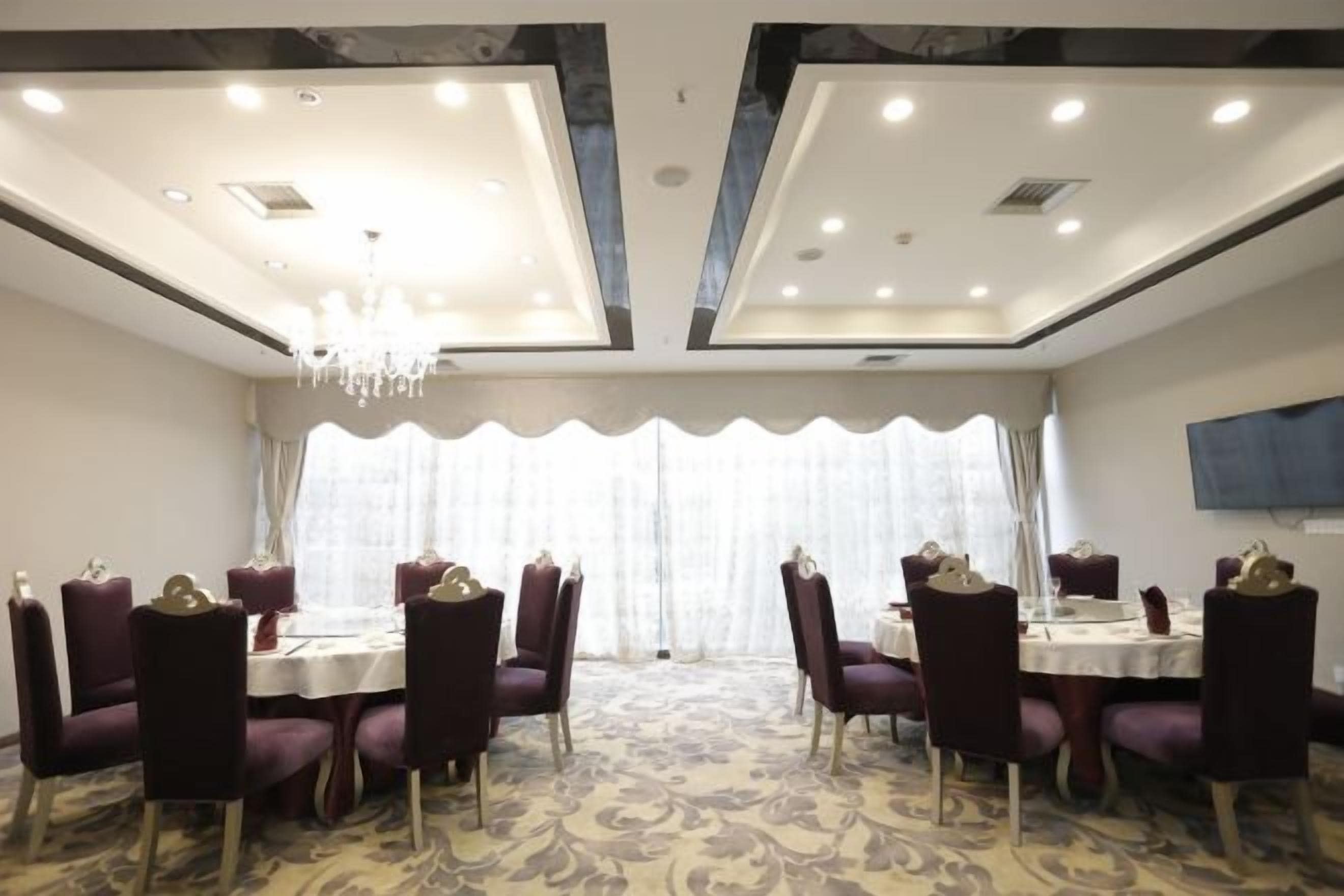 A conference room with round tables and chairs, a chandelier, and a large window with curtains.
