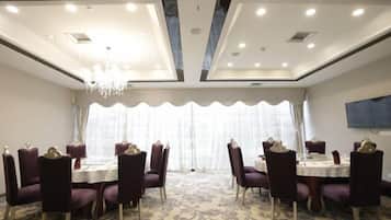A conference room with round tables and chairs, a chandelier, and a large window with curtains.