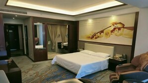 A hotel room with a bed, a massage chair, a desk, and a large painting on the wall. - Vienna International Hotel (Mount Emei Crystal Plaza Hotel) (Emeishan City)
