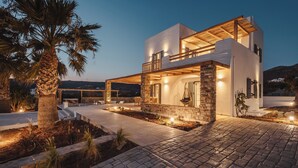A modern two-story house with a stone facade, a balcony, and a well-lit outdoor area. - Diamond of Cyclades (Kastraki)
