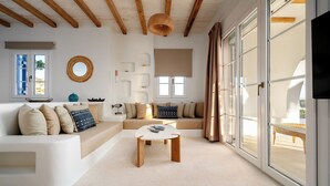 A modern living room with a white sofa, a coffee table, and a large window with curtains. - Diamond of Cyclades (Kastraki)