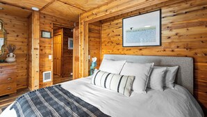 Dormitorio de una cabaña de madera con cama, almohadas, un cuadro enmarcado y un aparador.