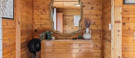 Interno di una casetta di legno con un comò, uno specchio e una ventola.