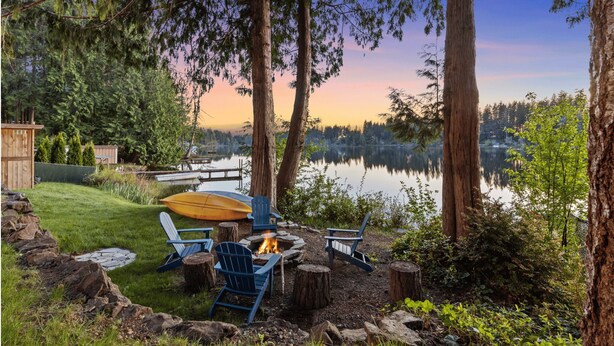 Un área de estar al aire libre frente al lago, con una chimenea, sillas y una canoa.