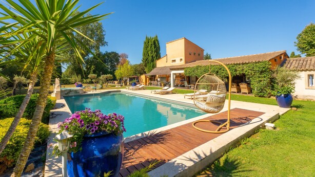 A swimming pool with a wooden deck, lounge chairs, and a hanging chair.