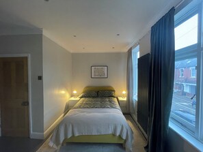 Cozy retreat with a single bed, bedside lamps, and a large window offering a view of the street.