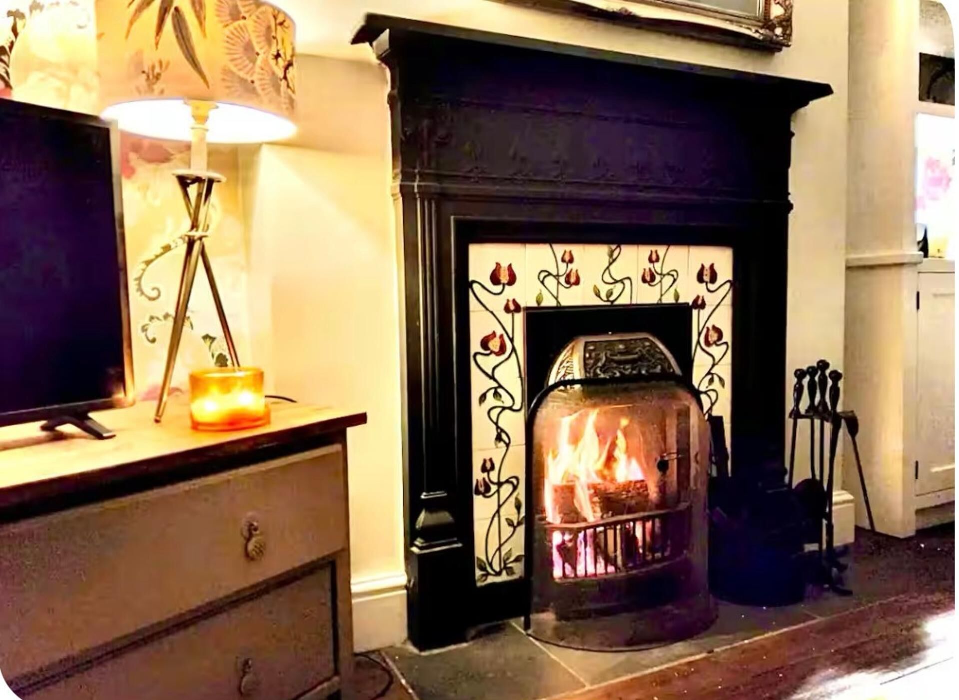 A fireplace with a fire, a television on a stand, and a lamp on a table.