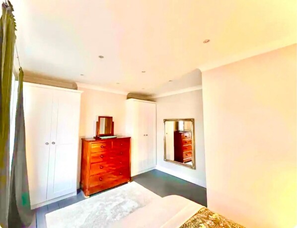A bedroom with a bed, a wooden dresser, a wardrobe, and a mirror on the wall. - Shepherds Bush W12 Magical Townhouse nr Westfield (London)