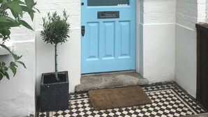 A blue door with a window above it, a small potted plant beside the door, and a checkered floor pattern. - Shepherds Bush W12 Magical Townhouse nr Westfield (London)