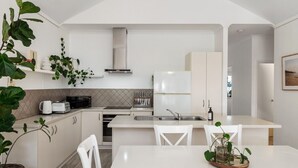 A modern kitchen with white cabinetry, a built-in oven, and a microwave. There is a dining area with a white table and chairs.