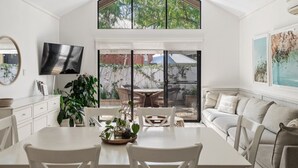 A modern kitchen with a dining area, large windows, and a TV mounted on the wall.