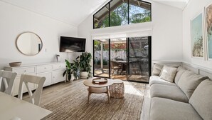 Un vaste salon doté d’un haut plafond, d’un grand téléviseur, d’un coin repas et d’une porte-fenêtre coulissante donnant sur une terrasse extérieure.