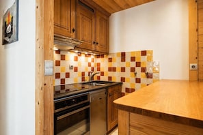 Cozinha com armários de madeira, painel de azulejos, pia de aço inoxidável e bancada de madeira.