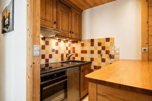 A kitchen with wooden cabinets, a tiled backsplash, a stainless steel sink, and a wooden countertop.