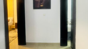Un couloir avec une œuvre d’art encadrée au mur, une porte donnant sur une pièce et un sol carrelé.