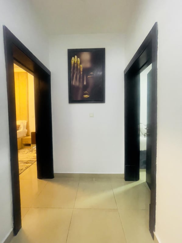 A hallway with a framed artwork on the wall, a door leading to a room, and a tiled floor.