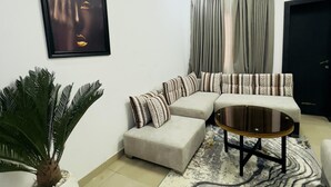 Un salon moderne avec un canapé d’angle, une table basse, une grande plante en pot et une œuvre d’art encadrée accrochée au mur.