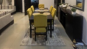 Un espace repas moderne avec une table ronde, des chaises jaunes et un meuble noir agrémenté d’objets décoratifs.