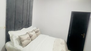 Une chambre à coucher avec un lit, des oreillers, une tête de lit, une porte et un luminaire.