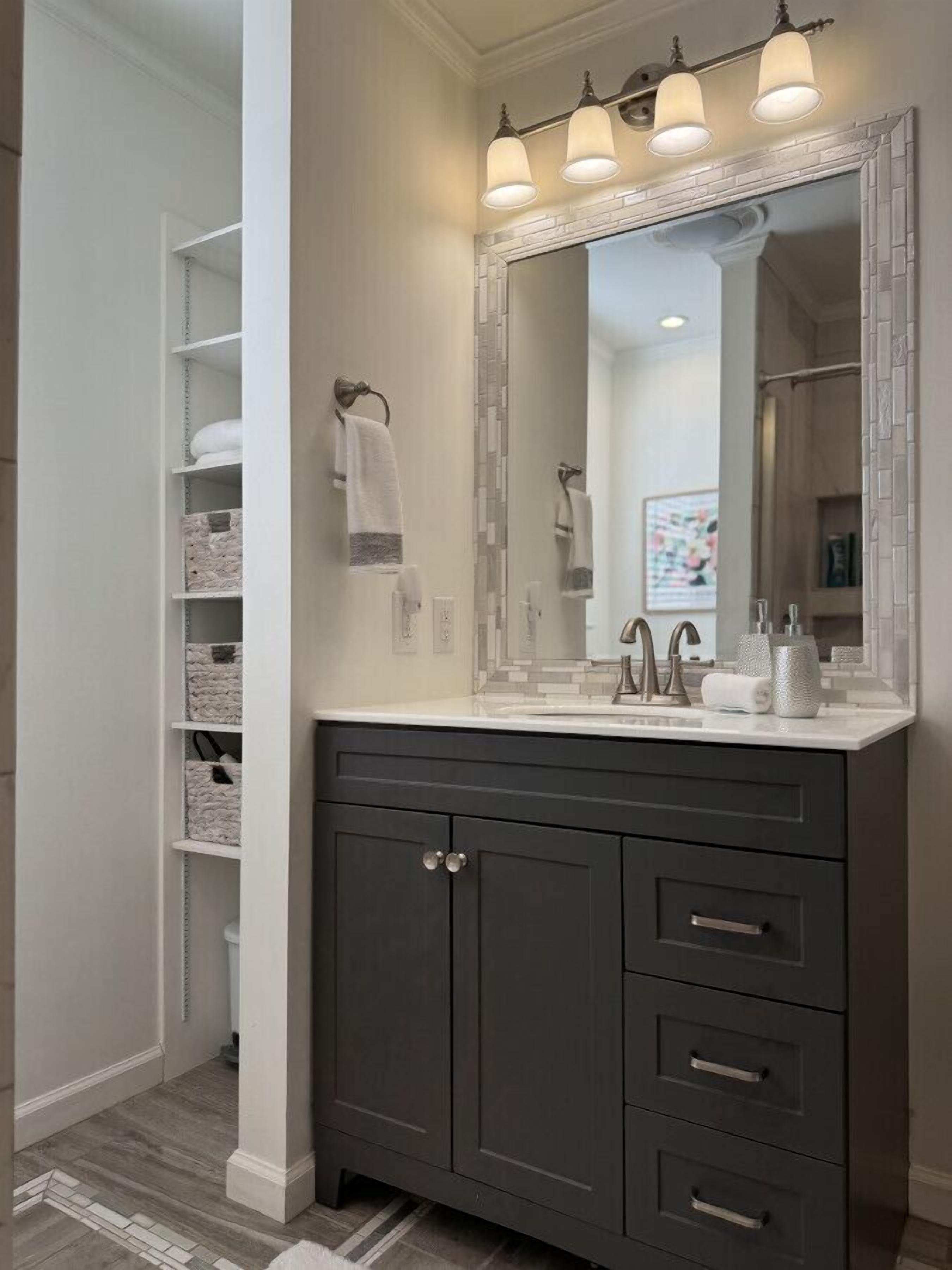 Une salle de bain avec un meuble-lavabo gris foncé, un grand miroir et trois appliques murales.