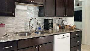 A modern kitchen with dark wood cabinets, a stainless steel sink, and a built-in dishwasher. - House at Guilford Hills (Greensboro)