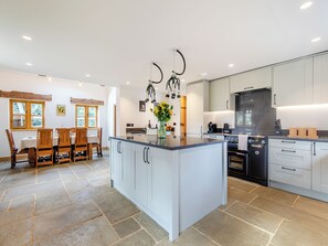 A modern kitchen with a large island, white cabinetry, and a dining area with wooden chairs and a table. - 4 bedroom accommodation in Whiteley Green, Macclesfield (Whiteley Green, Macclesfield)
